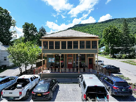 Historic two story building with porches on both levels, teal clapboard siding and restaurant on first floor. 